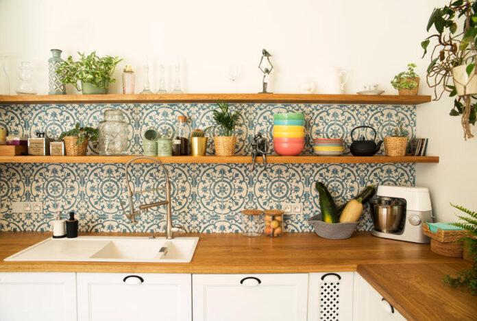 Kuchnia z białymi meblami, drewnianym blatem i półkami oraz patchworkowymi kaflami na ścianie